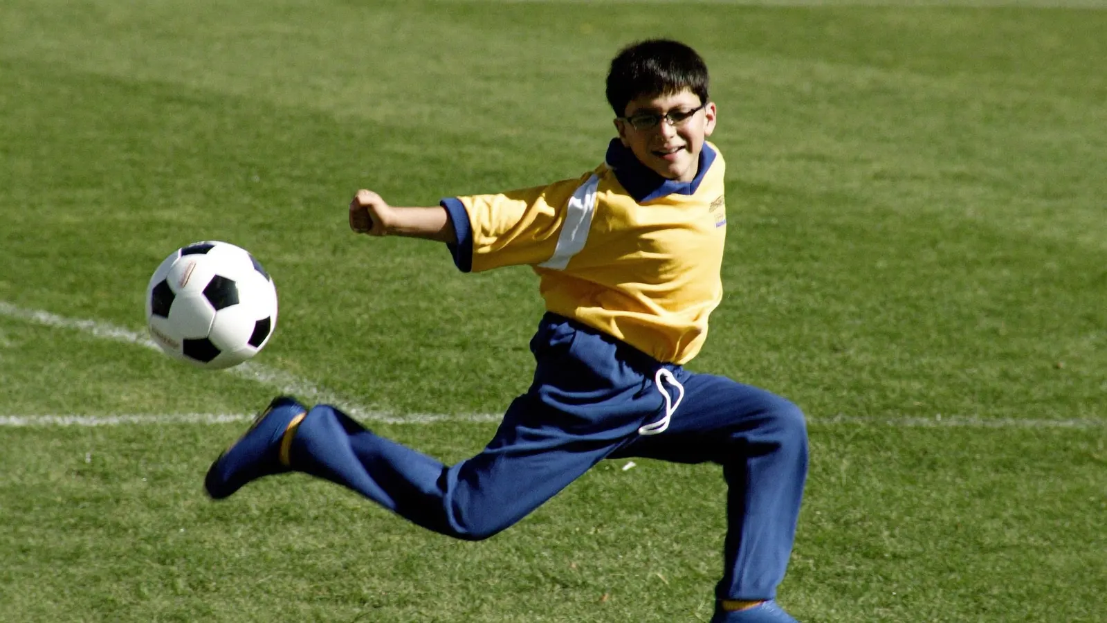 Ein Junge mit Brille schießt beim Fußballspielen auf einem Rasenplatz einen Ball.